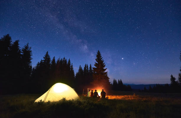 Tourists sitting near campfire under starry sky stock photo