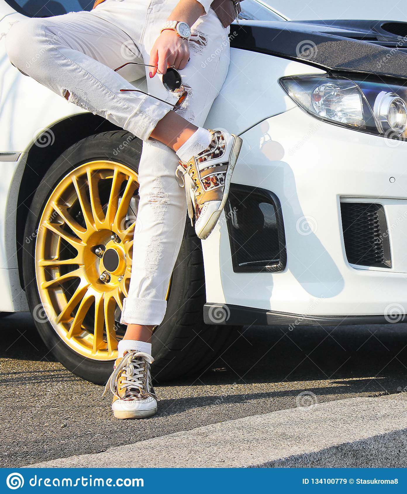 Girl in colored sneakers shoes and in white trousers on background of white car girl on car background stock image