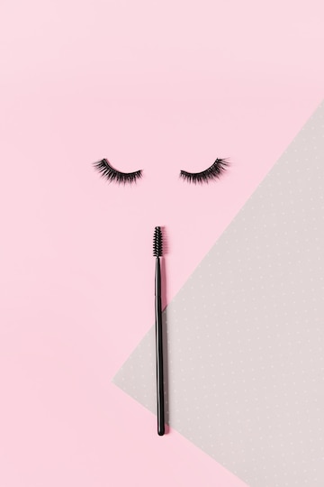 Premium photo creative layout with eyelashes and brush mascara closed eyes on pastel pink background