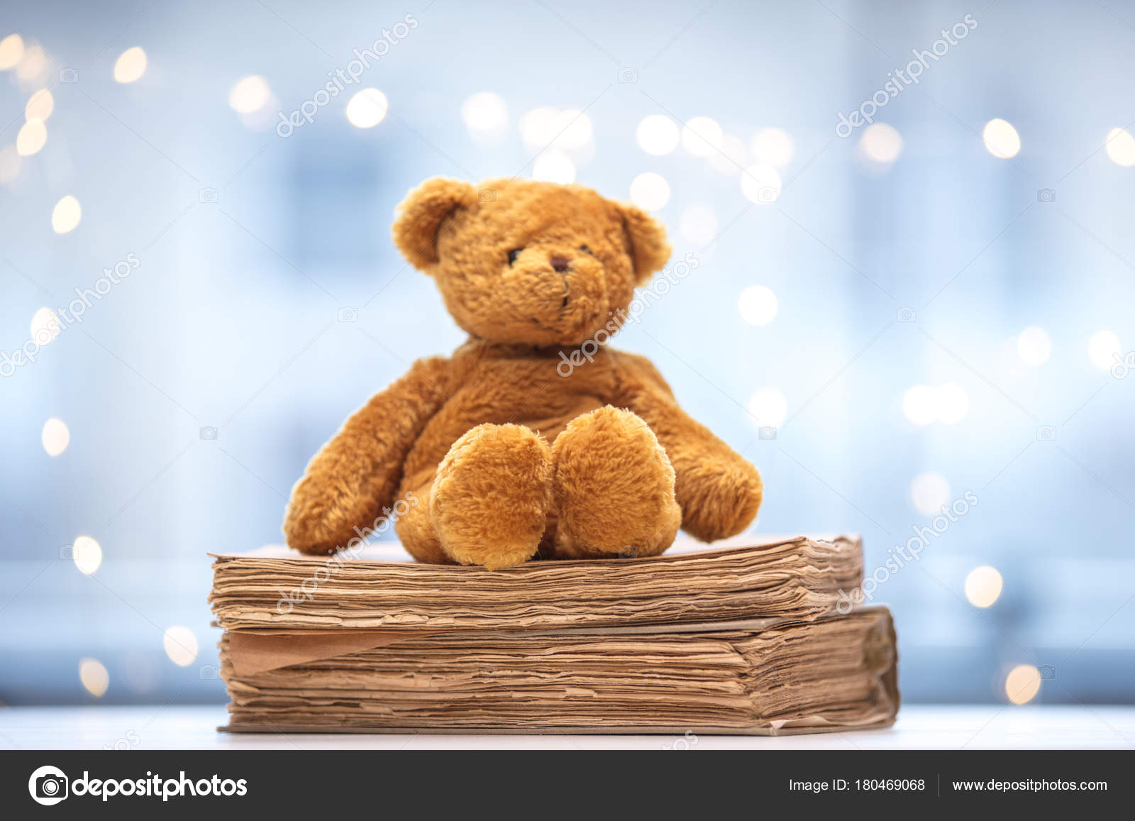 Teddy bear soft toy with old books on fairy lights stock photo by verasimon