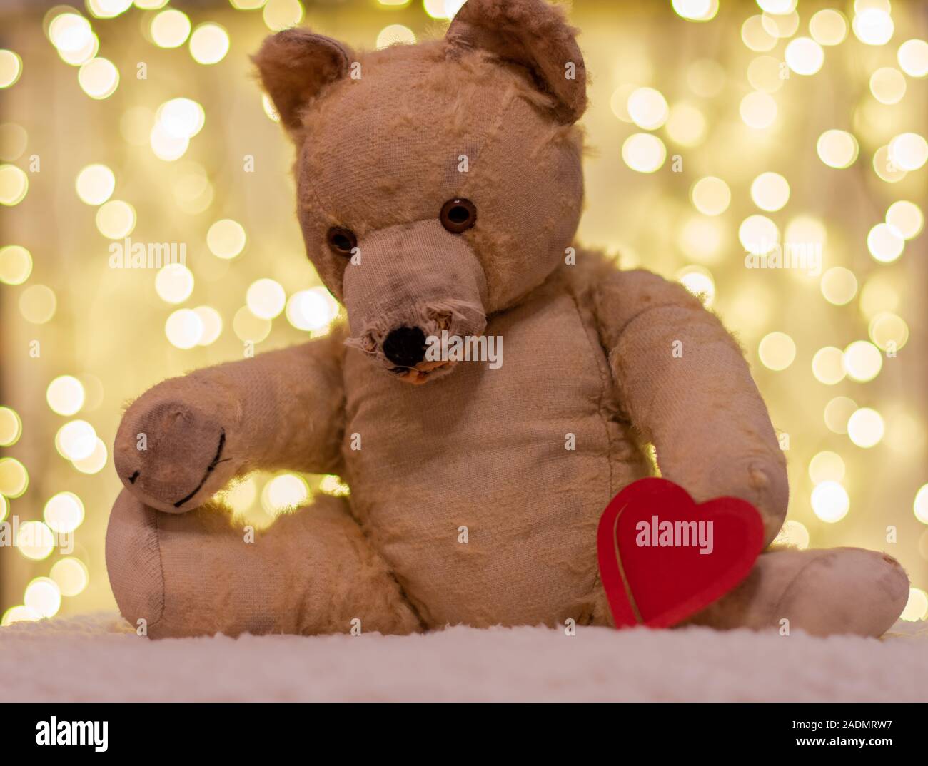 Very old soft toy between to years old teddy bear with red paper heart on the backdrop are christmas lights nostalgia love stock photo