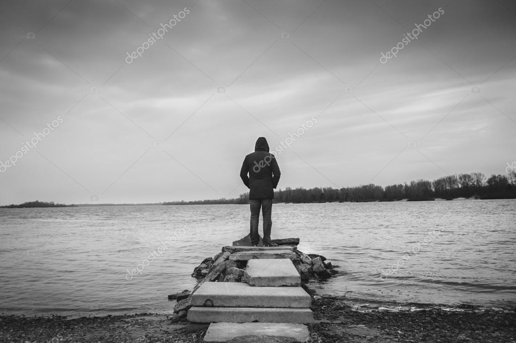 A man standing alone by the water stock photo by juliaberezovska