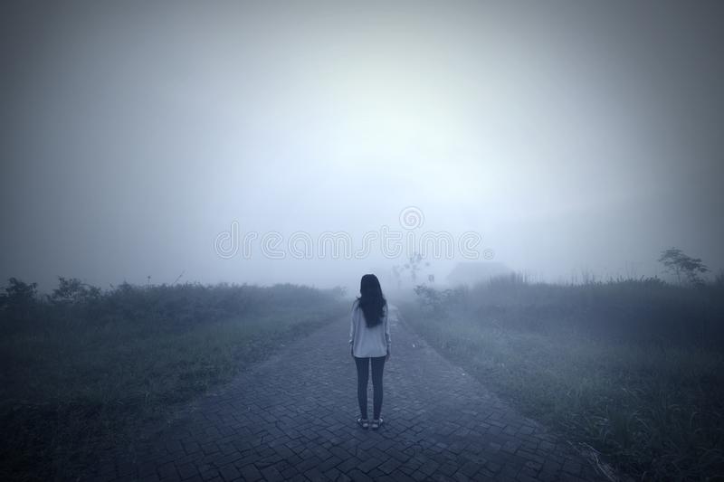 Sad woman standing alone in a misty morning stock photo