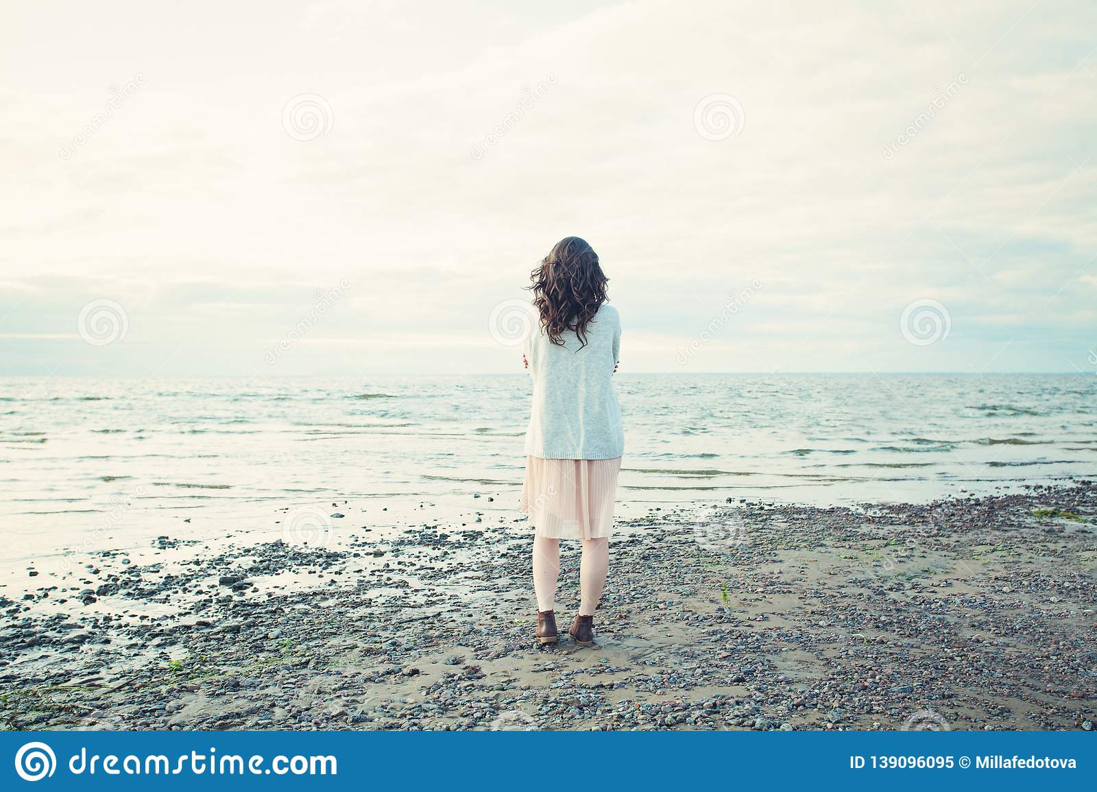 Beautiful girl standing alone on the coastline of the sea and looking at skyline romantic portrait stock image
