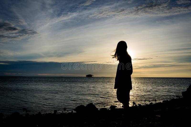 Silhouette of a girl standing alone on seashore with beautiful sky on the background stock image